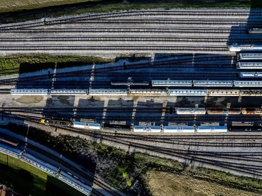 Aerial view of multiple parallel railway tracks with several freight trains parked, casting long shadows across the ground.