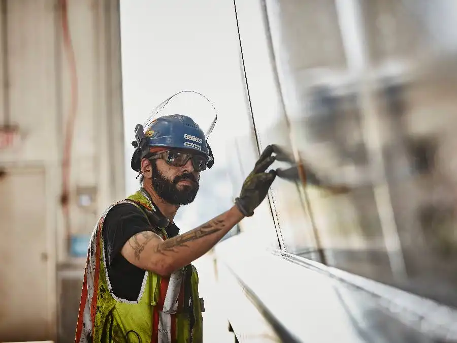 A construction worker wearing safety gear and a vest is inspecting or installing a glass panel inside a building.