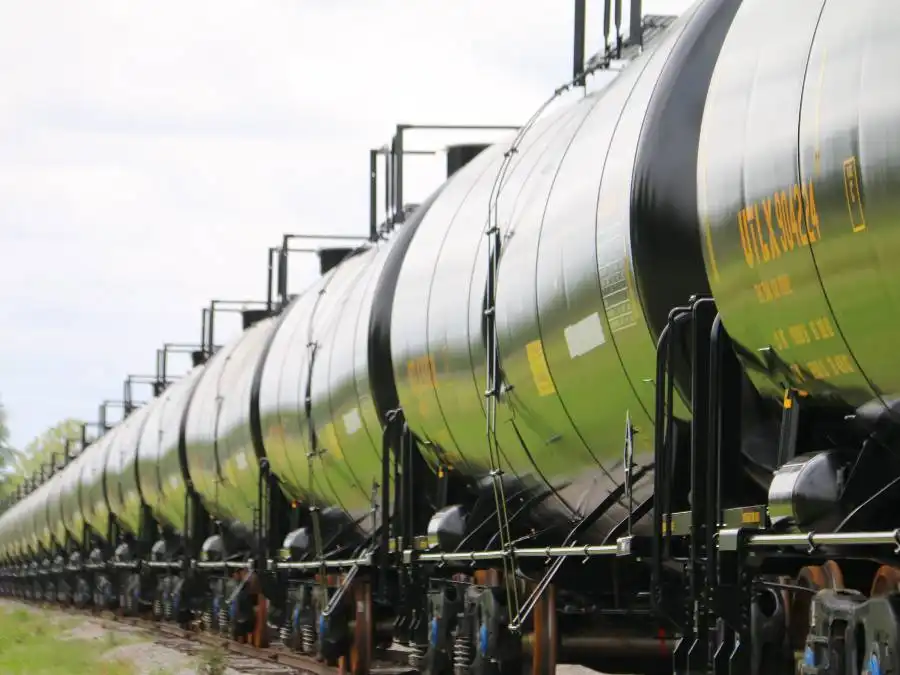 A row of black cylindrical tanker train cars on railroad tracks, shown from a low angle in daylight.